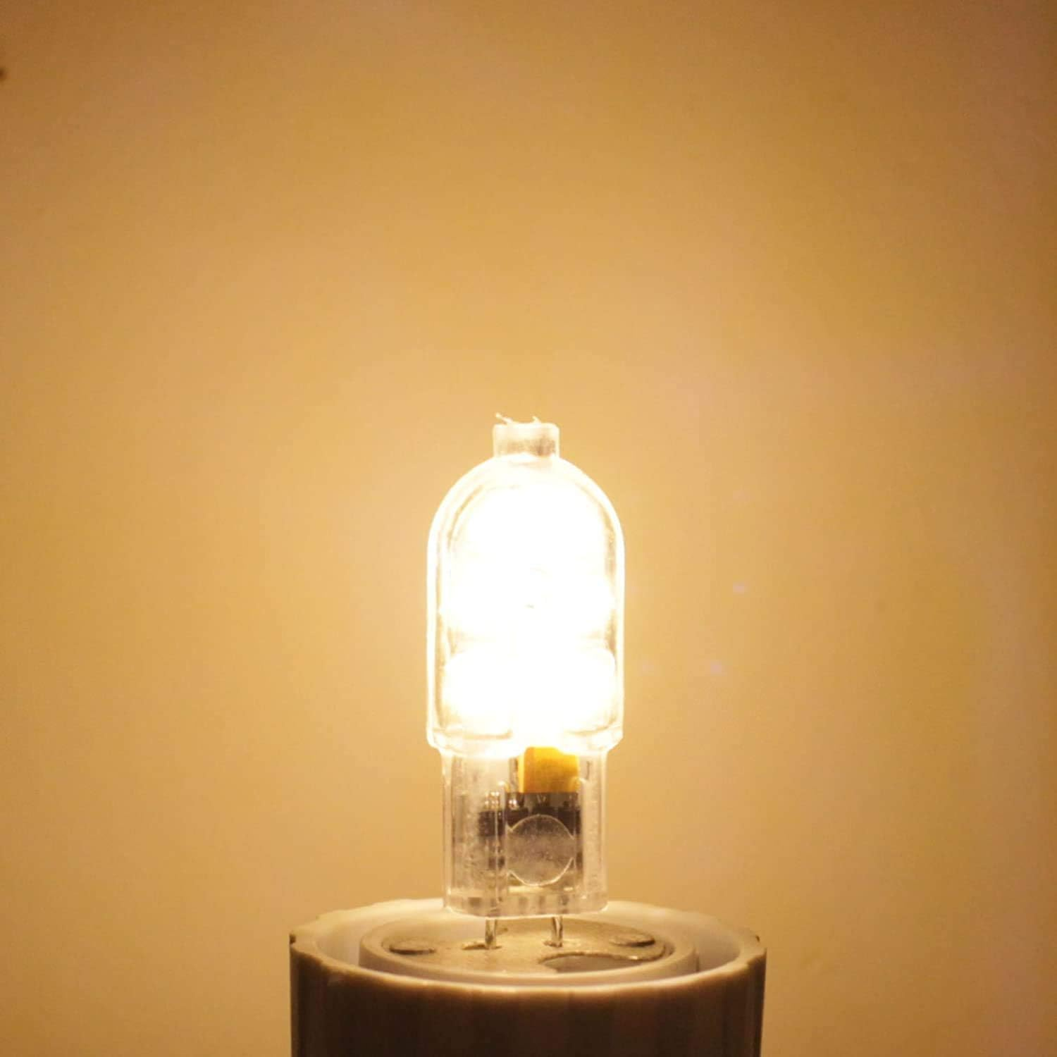 Eine eingeschaltete, helle Halogenlampe leuchtet auf einem Sockel vor gelbem Hintergrund.