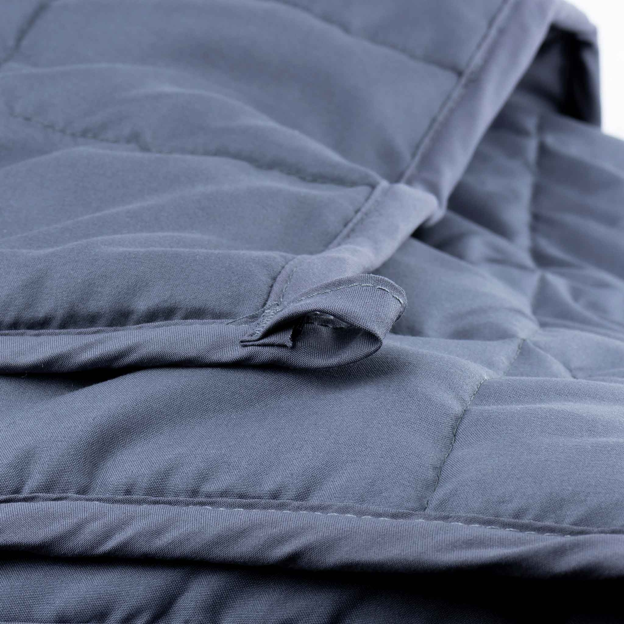 Nahaufnahme einer blauen, gesteppten Decke mit einer kleinen Stoffschlaufe am Rand.