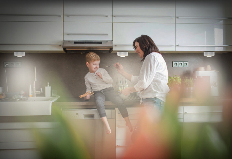 Een vrouw voedt een kind dat op het aanrecht in een moderne keuken zit.