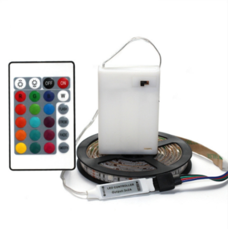 LED-Streifen auf Spule mit weißem Controller und Fernbedienung mit vielen bunten Tasten vor weißem Hintergrund.