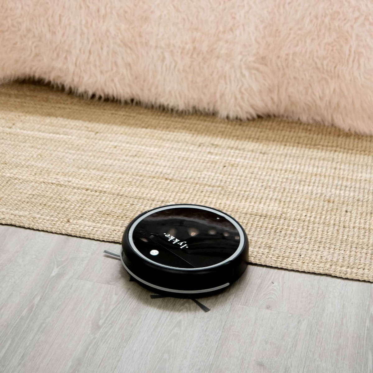 Ein schwarzer Saugroboter reinigt einen Holzboden vor einem Teppich.