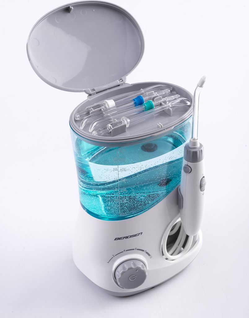 Ein weiß-grauer Munddusche mit blauem Wassertank, offenem Deckel, Aufsätzen oben und Bedienteil unten.