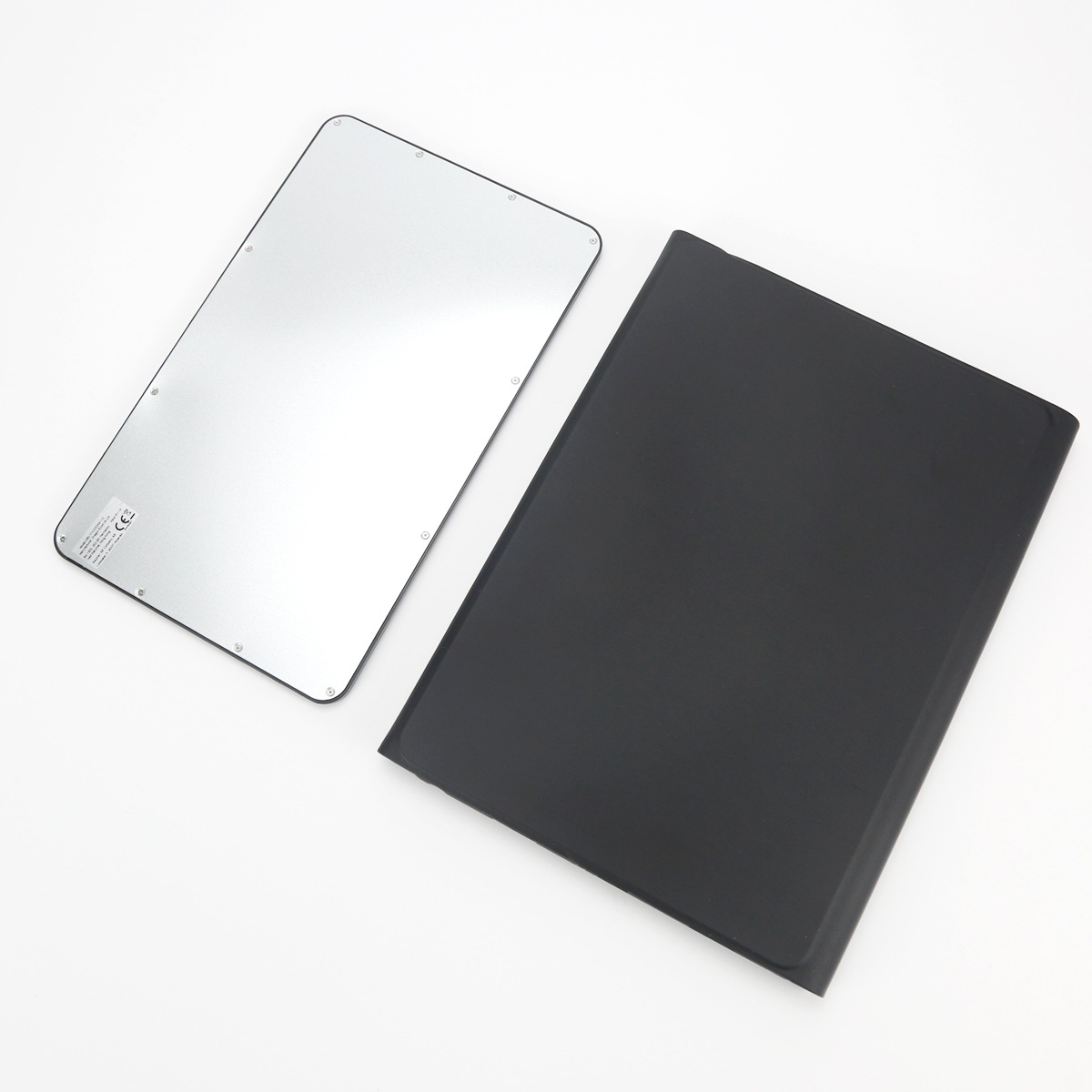 Il retro di un tablet argentato con viti e una custodia protettiva nera giacciono affiancati su sfondo bianco.