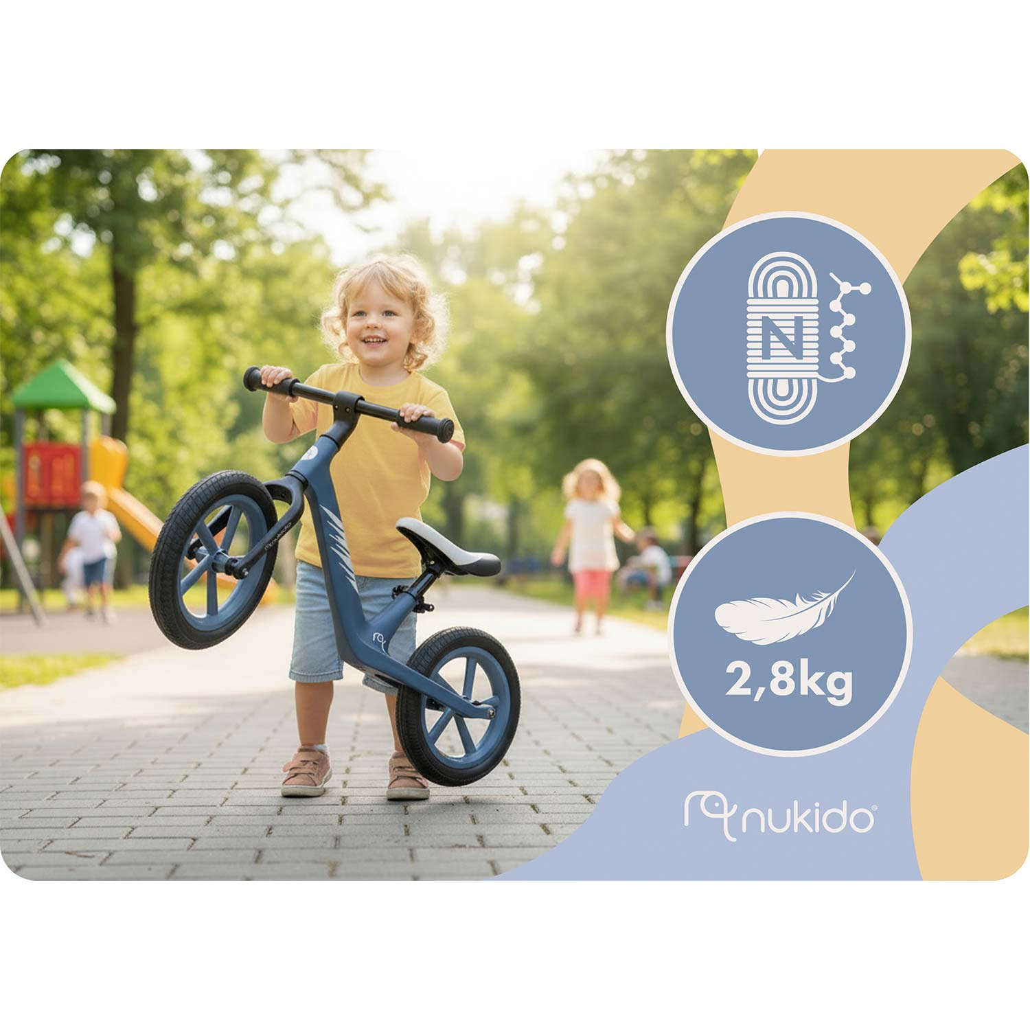 Maluch radośnie podnosi niebieski rowerek biegowy w słonecznym parku.