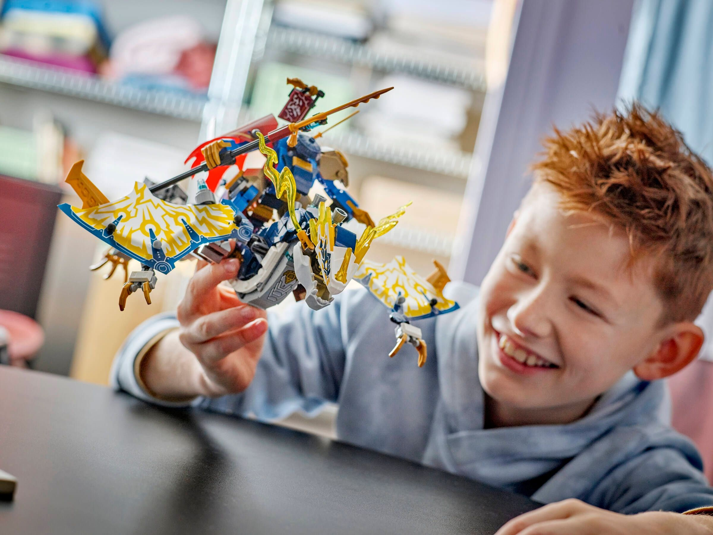 Un ragazzo sorridente che tiene un giocattolo drago LEGO blu e oro.