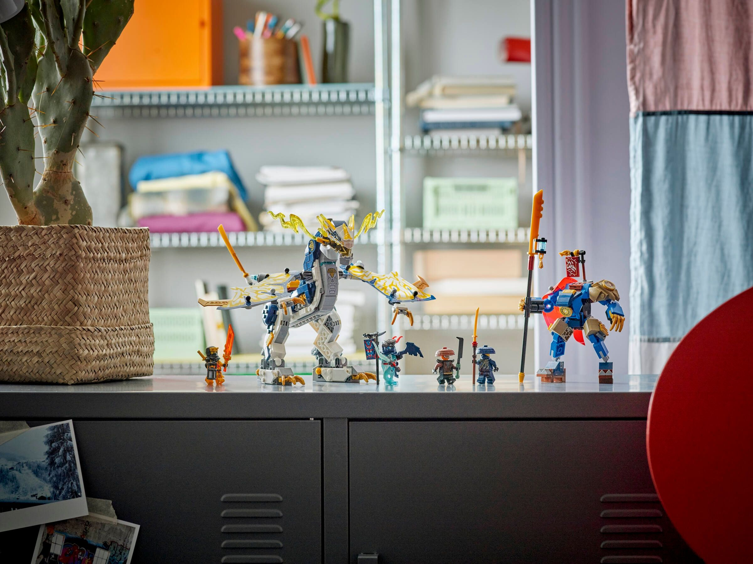 Personaggi Lego Ninjago e un drago su un mobile grigio davanti a uno scaffale.