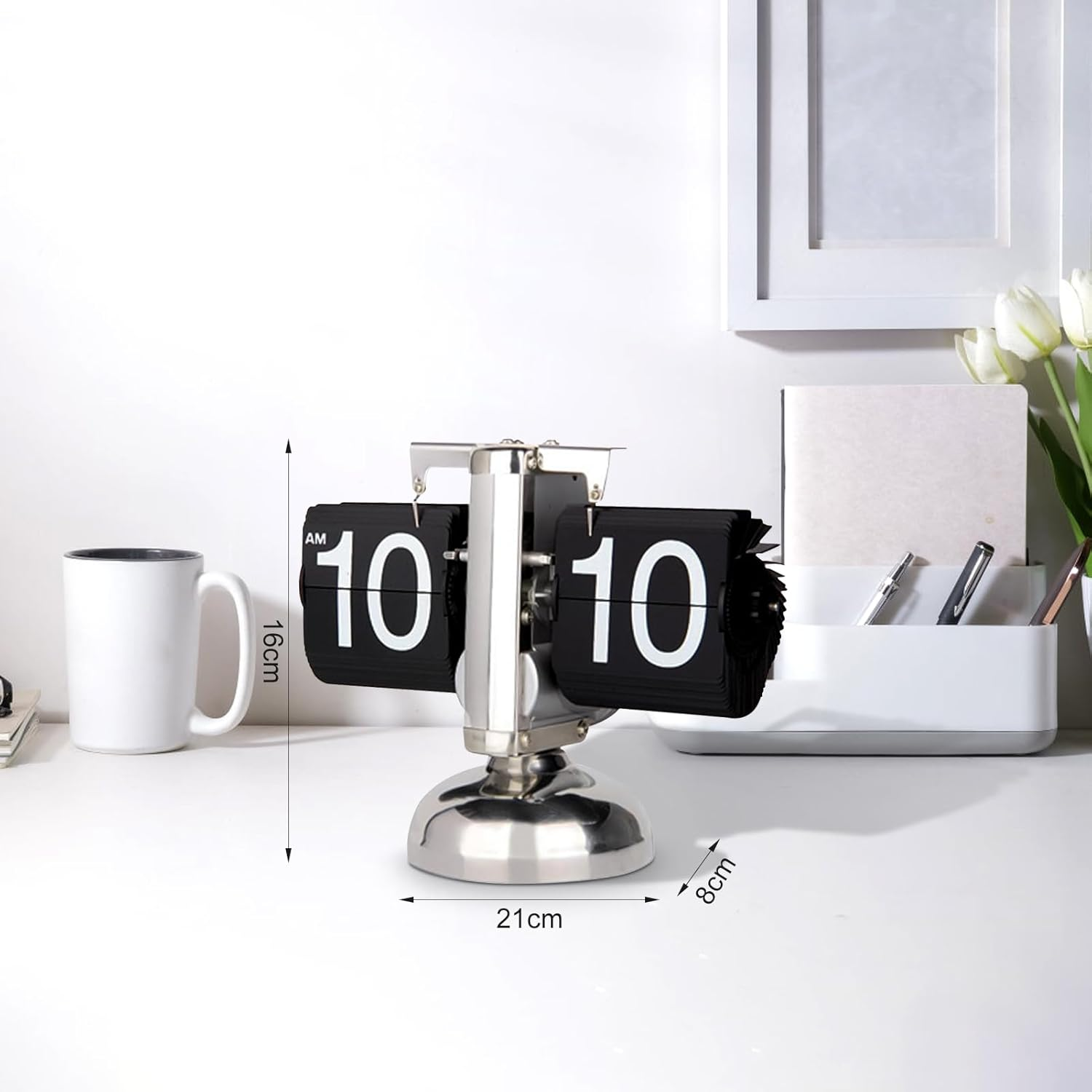 Eine silberne Flip-Uhr zeigt 10:10 auf einem weißen Schreibtisch mit Tasse und Stiftehalter.