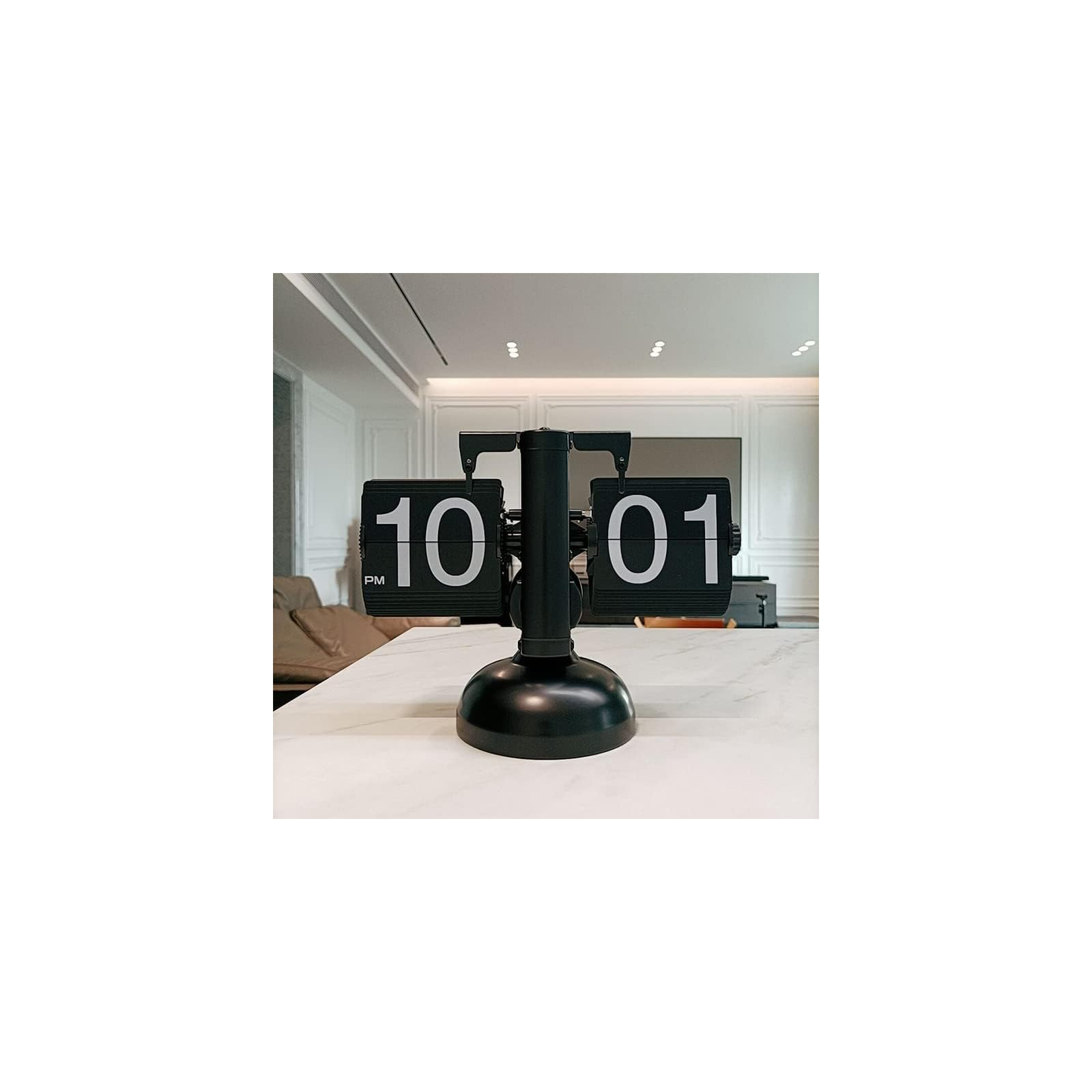 Eine schwarze Tisch-Flip-Uhr auf einer weißen Oberfläche in einem modernen Raum zeigt 10:01 PM.