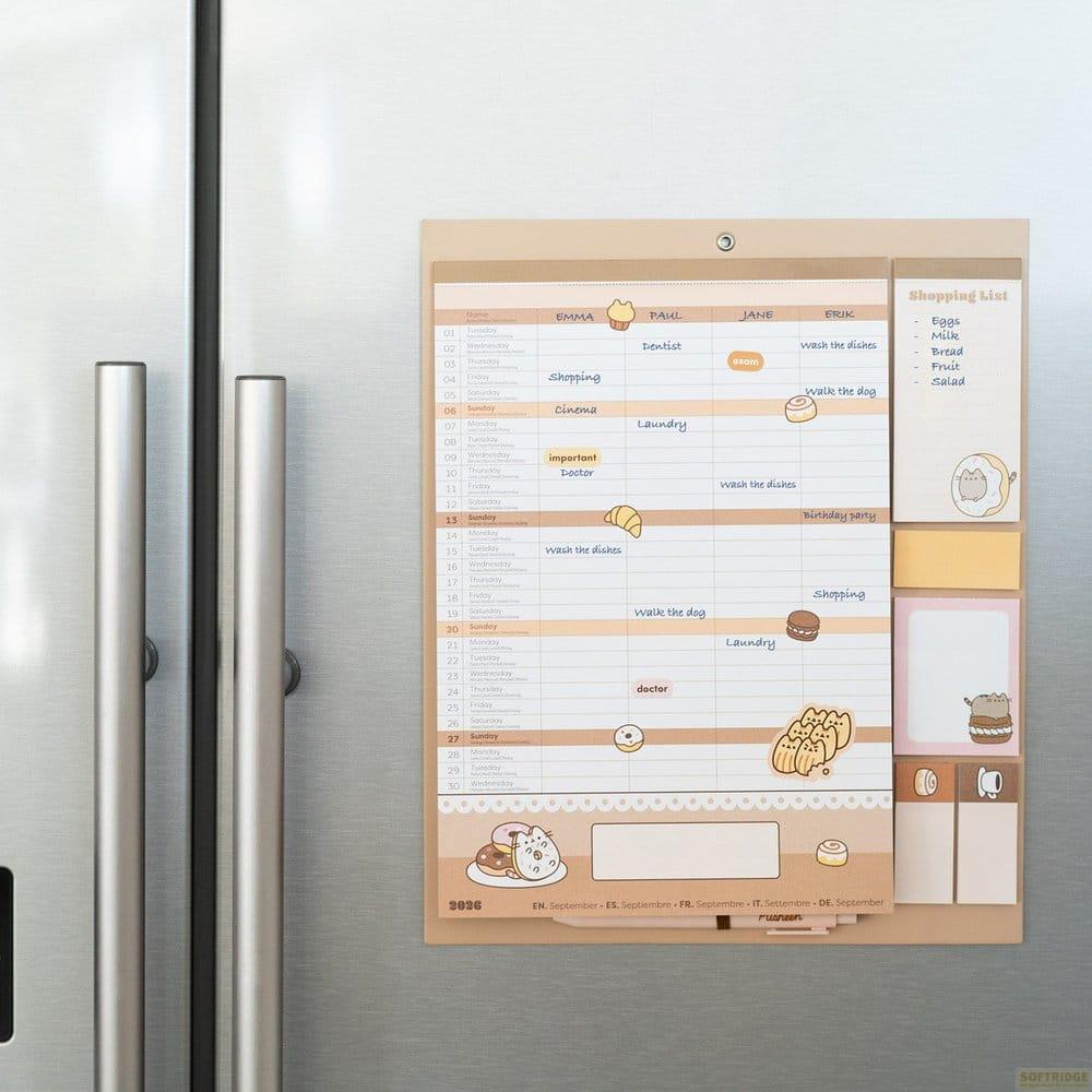 Un calendario familiar y una lista de compras están unidos con un imán a la puerta de un refrigerador plateado.