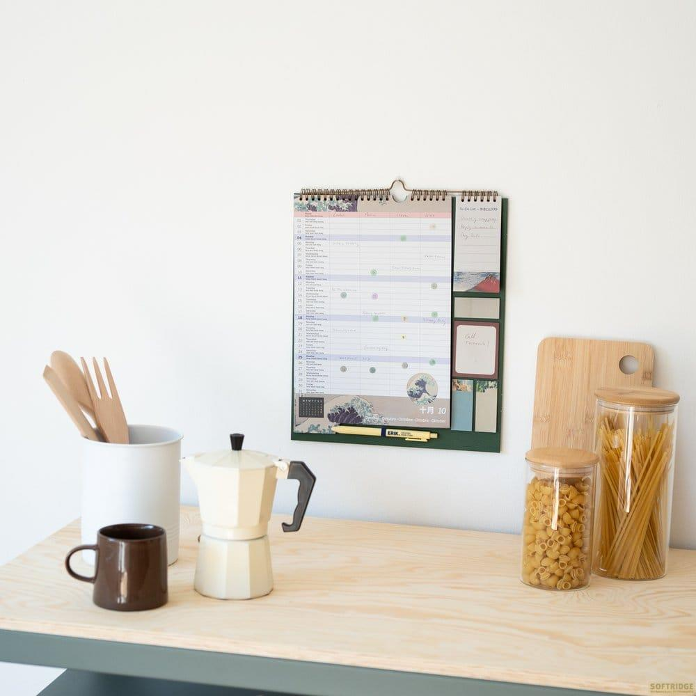 Calendario de pared sobre un escritorio de madera con cafetera, taza, utensilios y tarros.