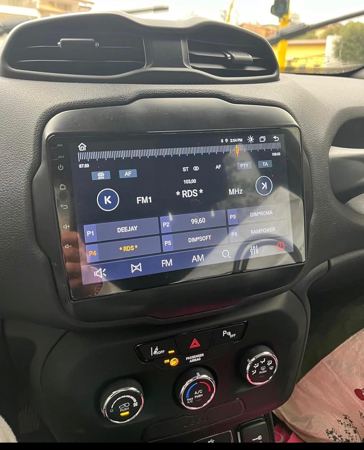 Cruscotto auto con touchscreen multimediale digitale che mostra le stazioni radio FM e manopole di controllo.