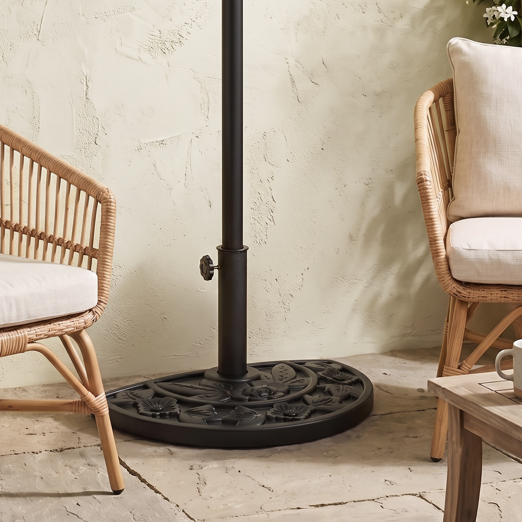 Una base de sombrilla negra con patrón floral descansa en un patio entre dos sillas de ratán.