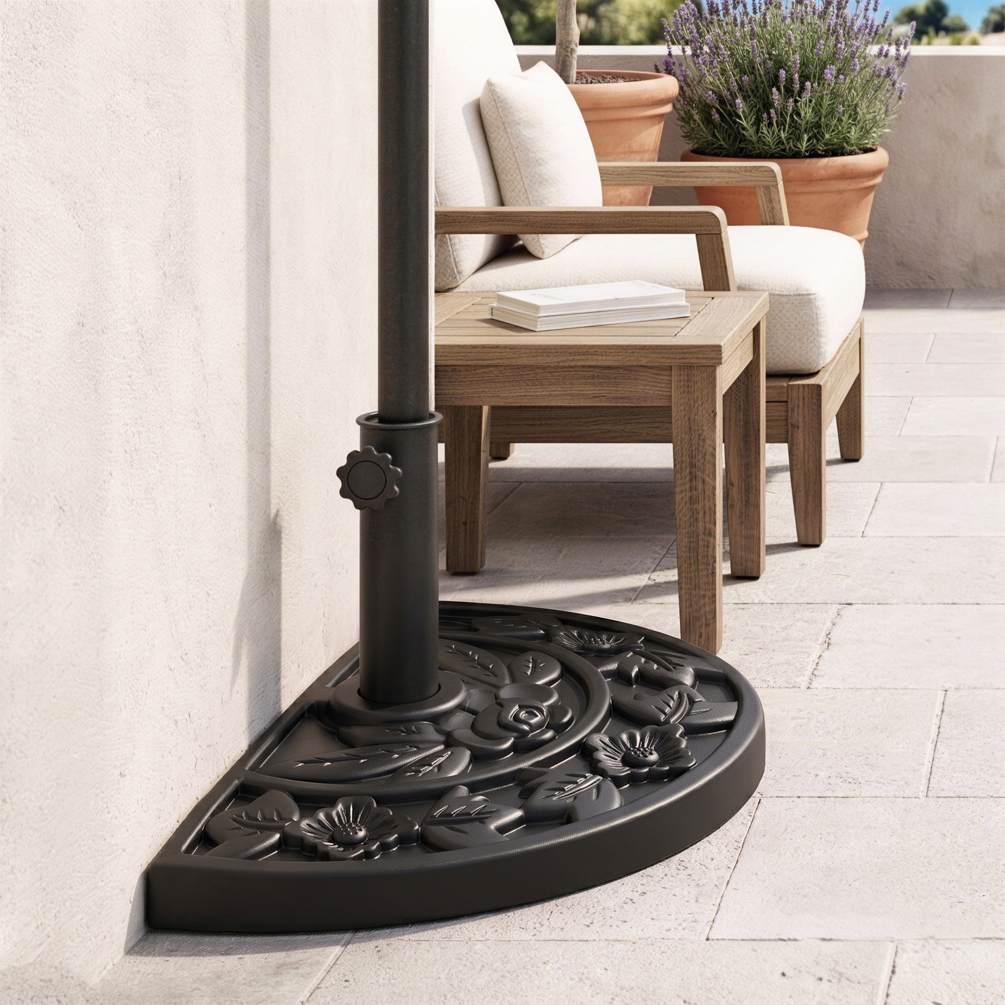 Una base de sombrilla negra de medio círculo con motivos florales descansa en un patio junto a una silla de madera y plantas.