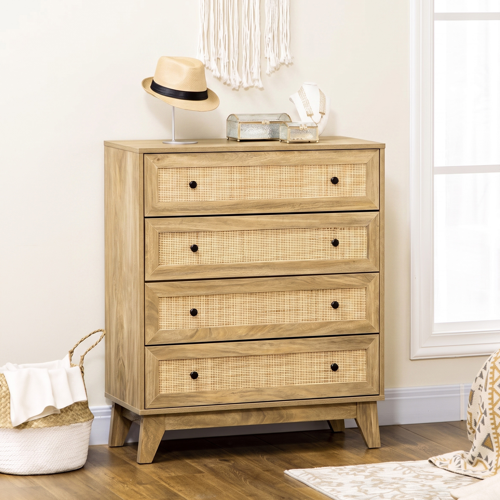 Una cómoda de madera de cuatro cajones con paneles de mimbre se encuentra contra una pared neutral con un sombrero y cajas.
