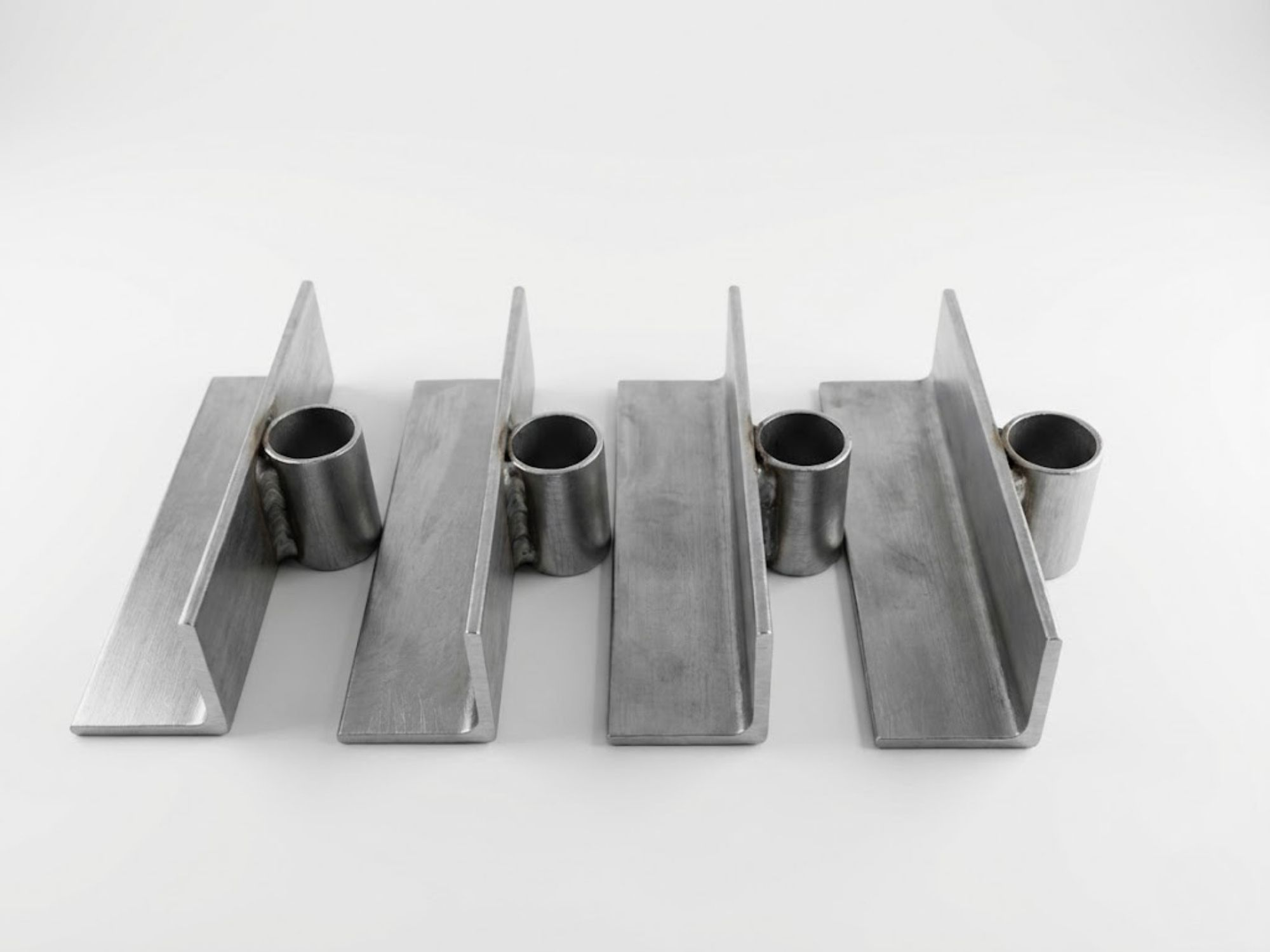Vier silberne Metallteile aus Winkeleisen und kurzen Röhren auf weißem Grund.