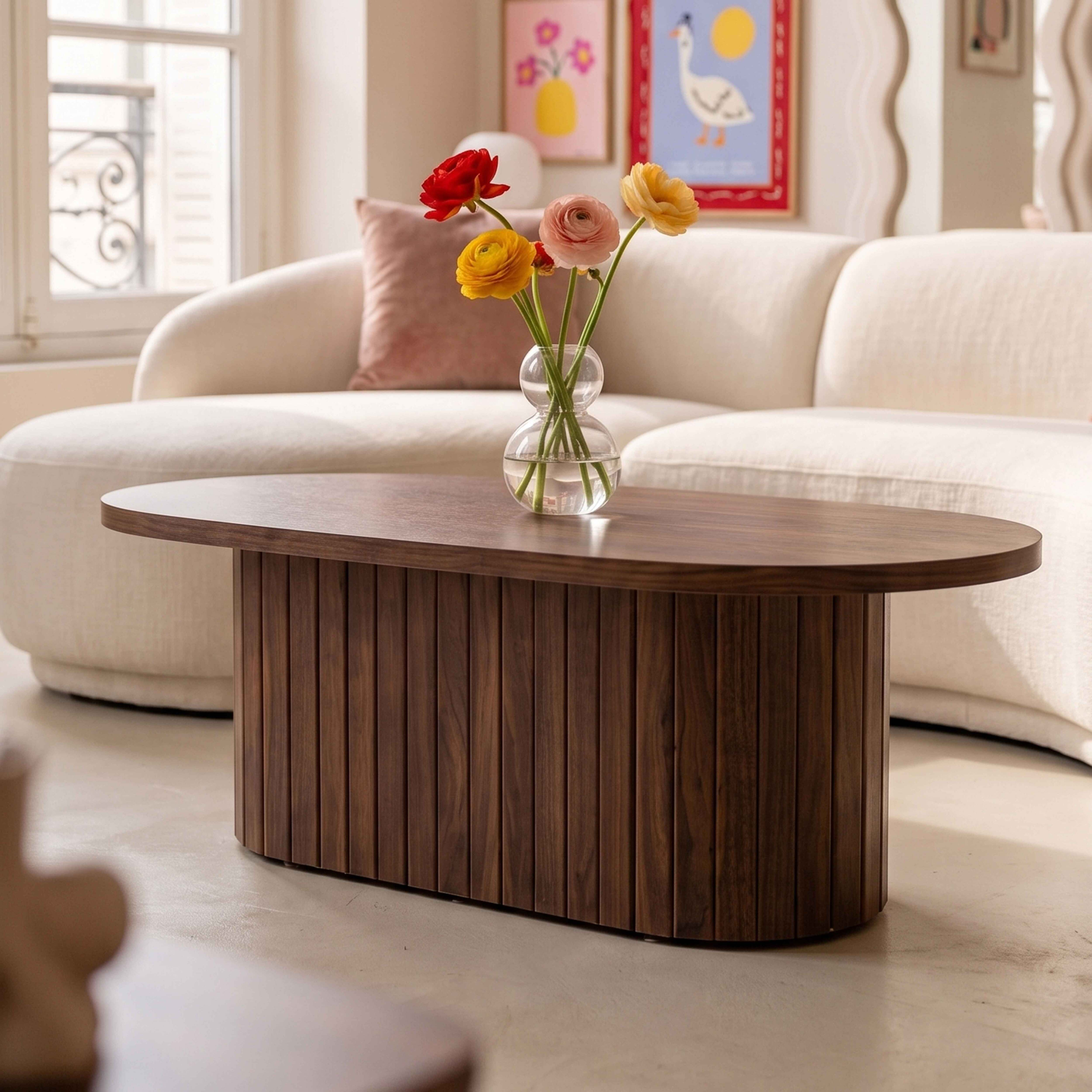 Ein hölzerner Couchtisch mit einer Blumenvase steht in einem hellen Wohnzimmer vor einem großen weißen Sofa.