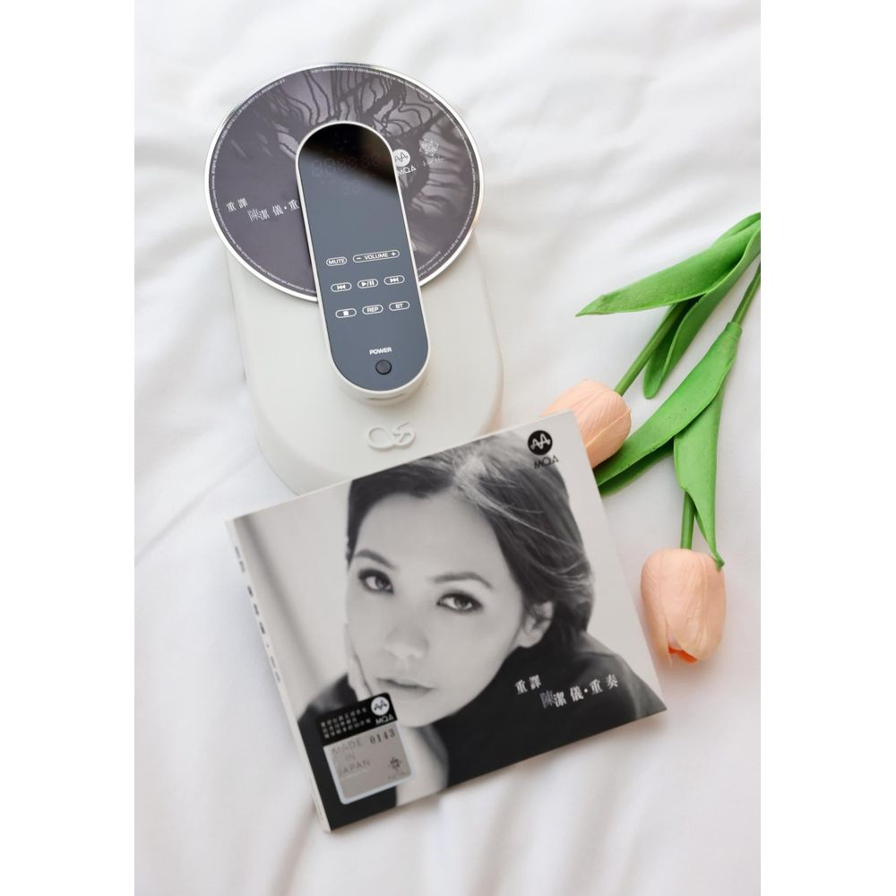 Un reproductor de CD blanco con control remoto, folleto y tulipanes rosas en una cama blanca.