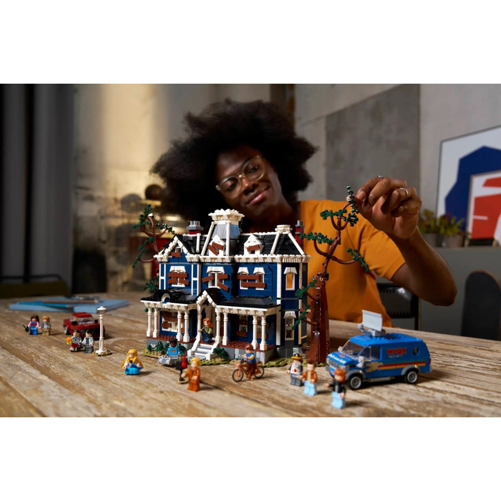 Una persona costruisce un dettagliato set Lego di una casa stregata blu con minifigure e un furgone.