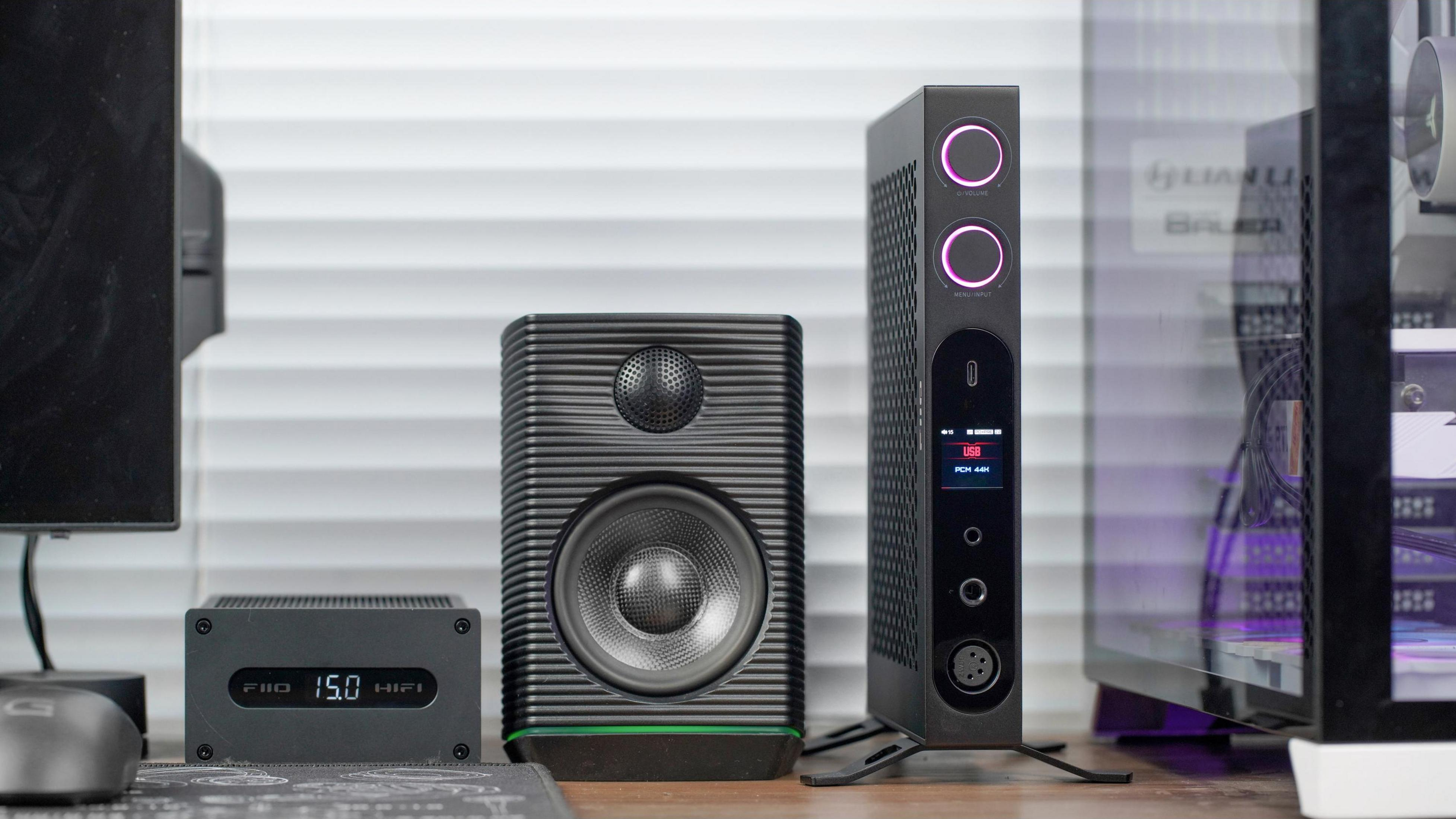 Varios equipos de audio, incluido un amplificador FiiO, un altavoz negro y un DAC delgado, dispuestos en un escritorio.