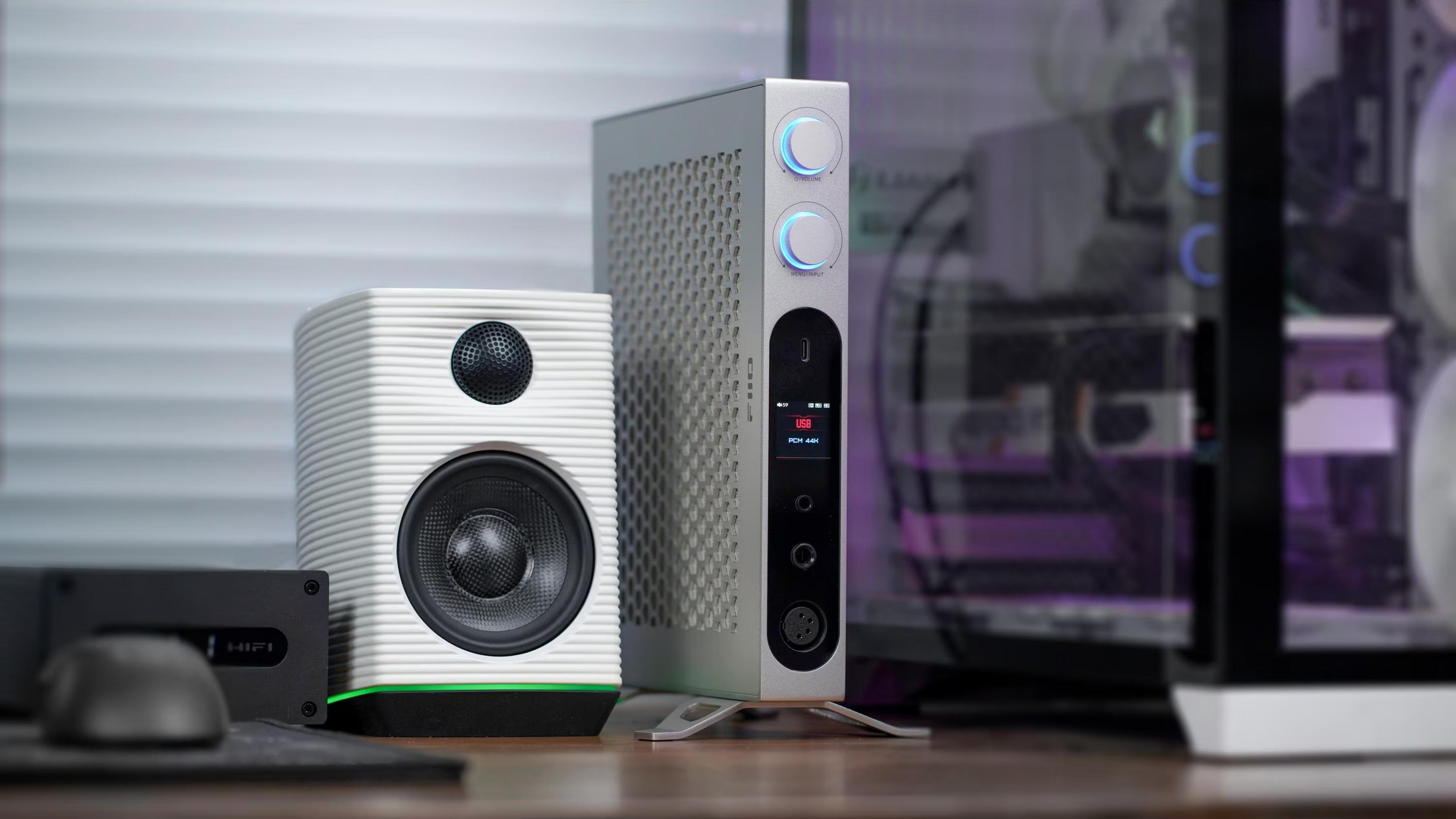 Un dispositivo de audio vertical plateado con perillas azules, un altavoz blanco estriado y una torre de PC.