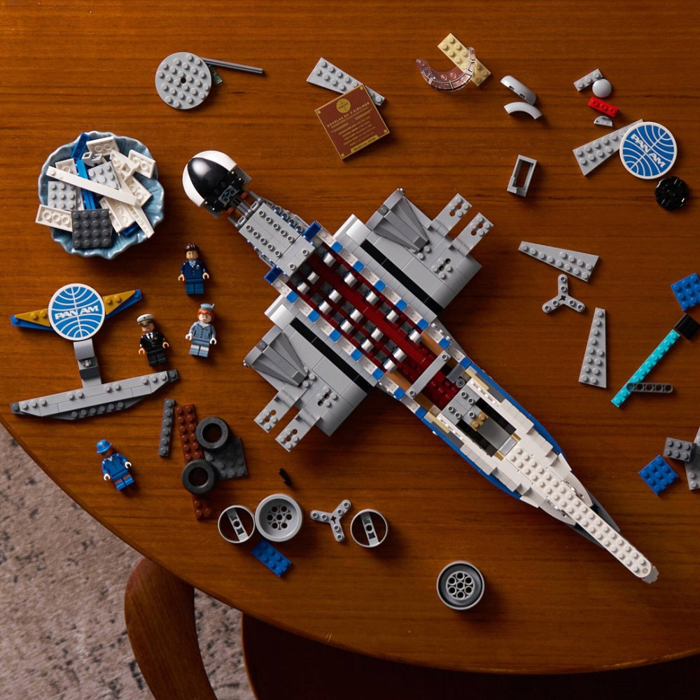 Widok z góry na częściowo zbudowany model samolotu Lego Pan Am i rozrzucone klocki na drewnianym stole.