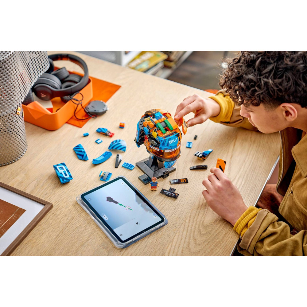 Un joven construye un colorido casco de coche de carreras Lego en una mesa de madera con una tableta.