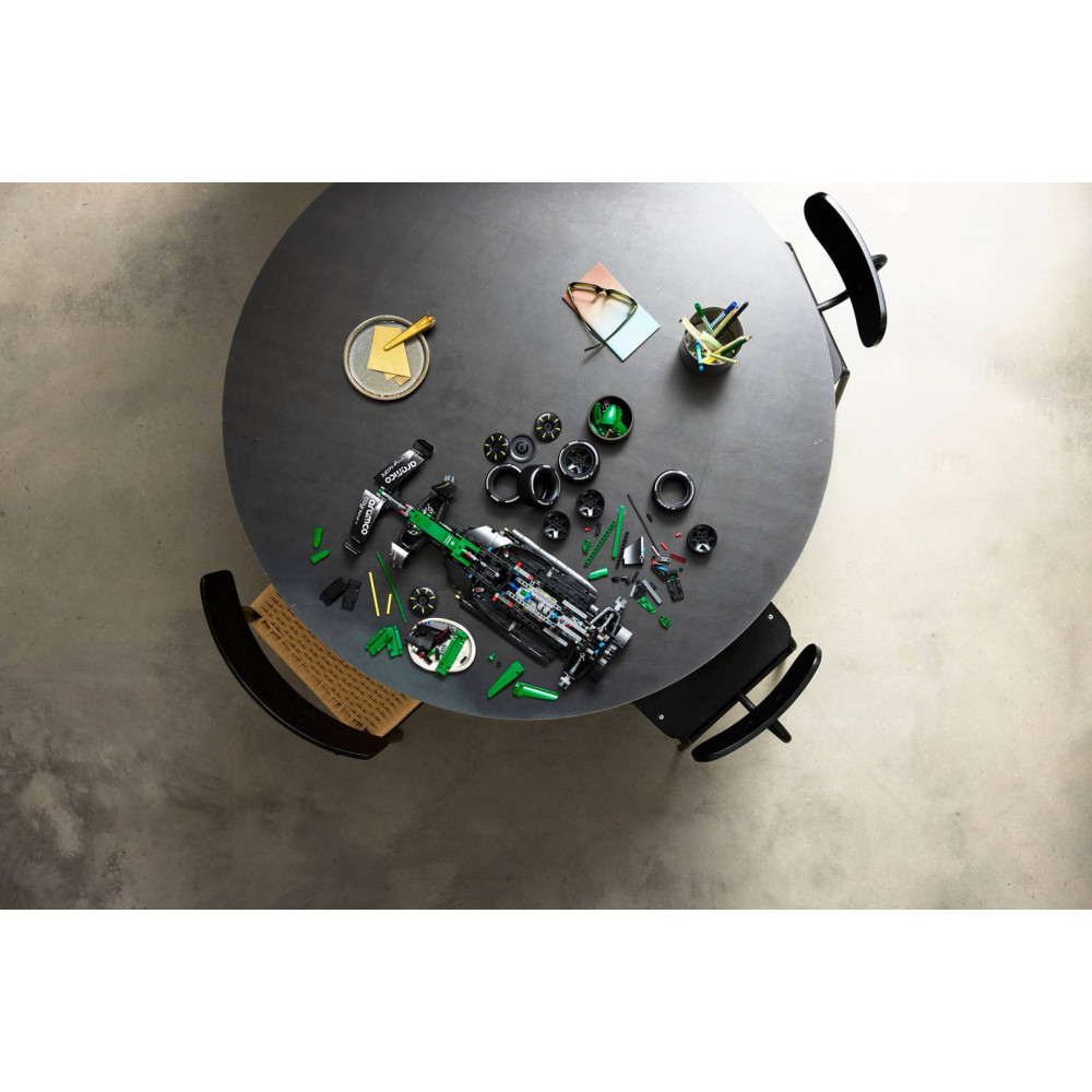 Eksik bir Lego Formula 1 aracı, yedek parçalar, kalemler ve gözl ük olan yuvarlak masanın yukarıdan görünümü.