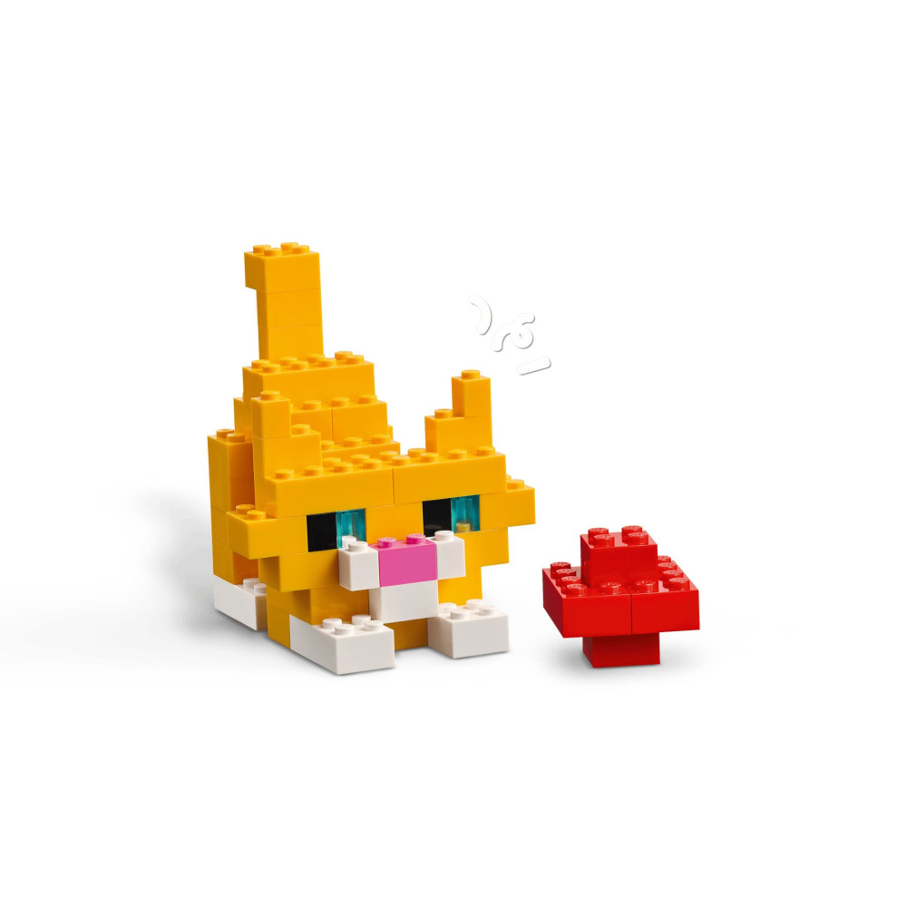 Pomarańczowy kot z klocków Lego z białym pyszczkiem i łapkami stoi obok małego czerwonego grzybka.