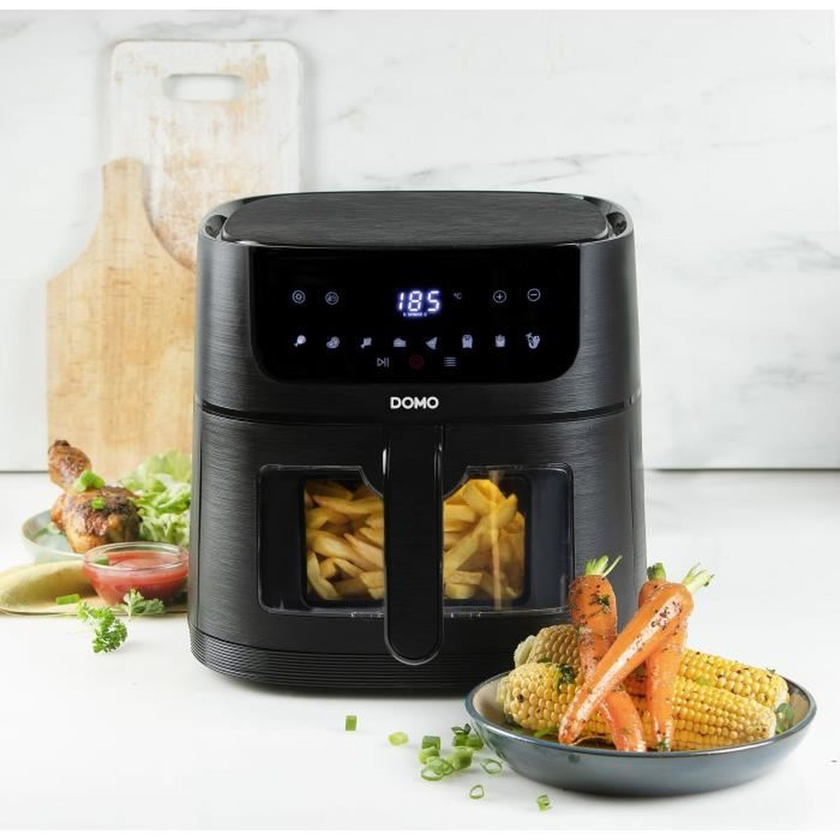 Friggitrice ad aria nera con display digitale su un bancone, affiancata da cibo e taglieri.
