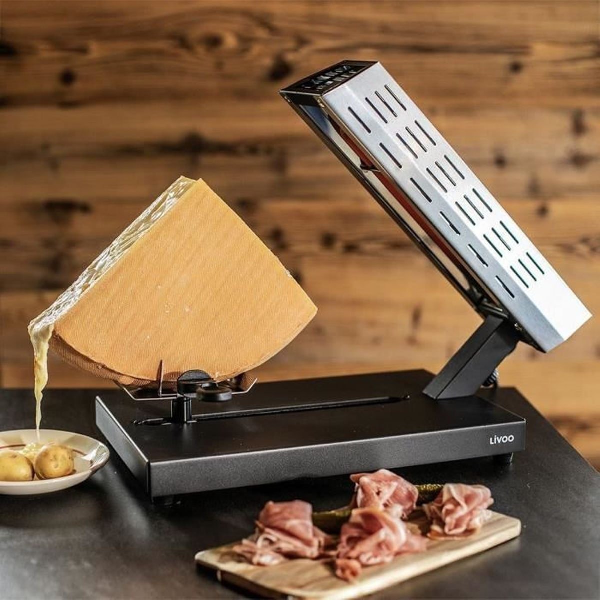 Una macchina per raclette scioglie il formaggio vicino a patate e prosciutto.