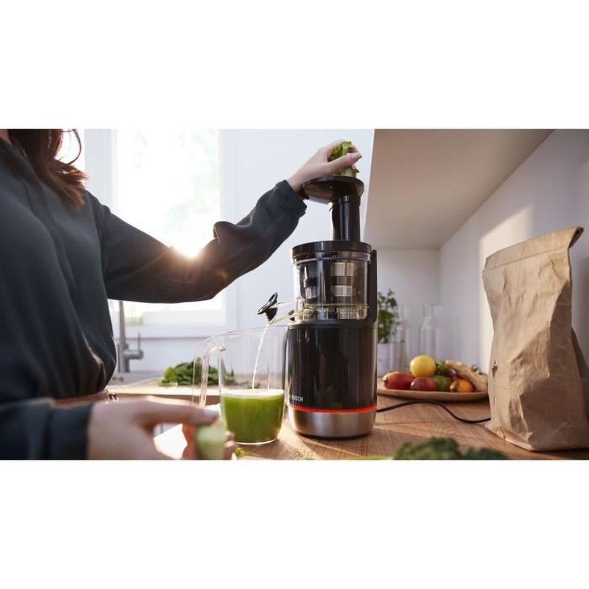 Una donna usa una centrifuga nera in una cucina luminosa mentre il succo verde scorre.