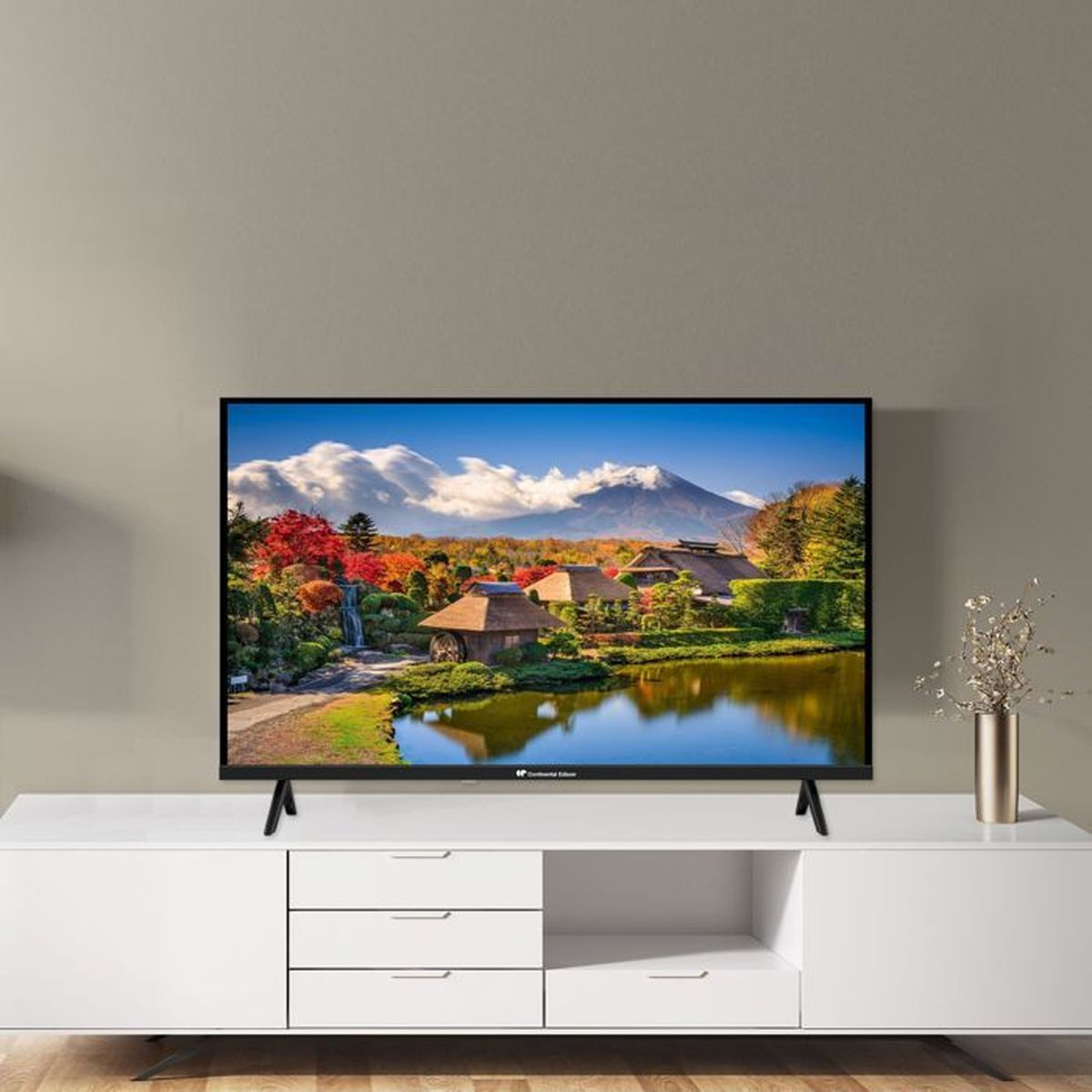 Una TV su un mobile bianco mostra un paesaggio montano giapponese con un lago e case tradizionali.