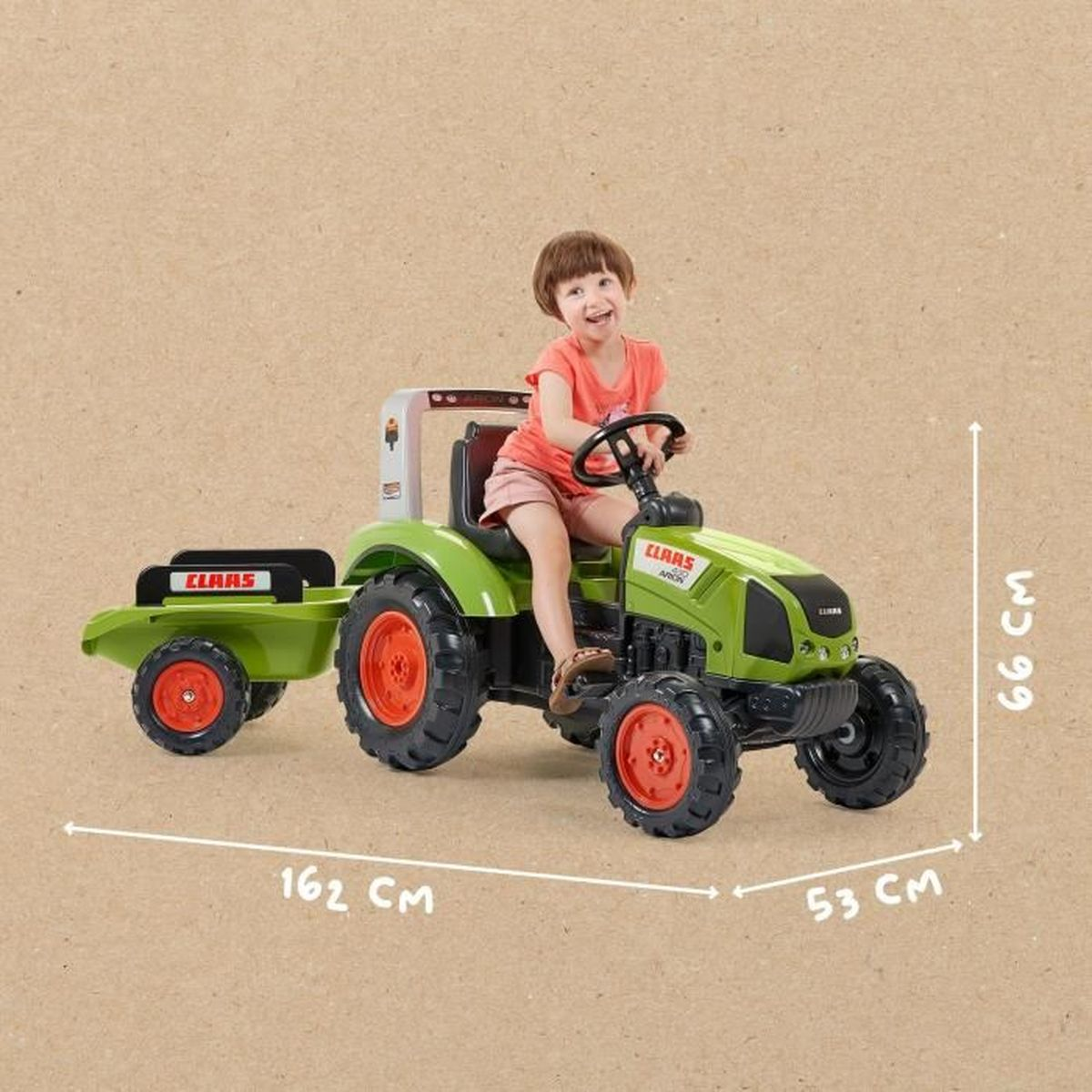 Kind sitzt auf einem grünen Spielzeugtraktor mit Anhänger, inklusive Maßangaben vor beigem Hintergrund.