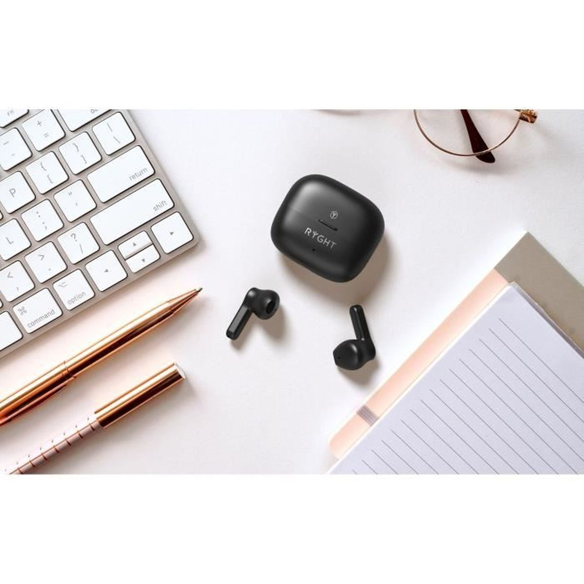 Auricolari wireless neri con custodia di ricarica su una scrivania bianca con tastiera e taccuino.