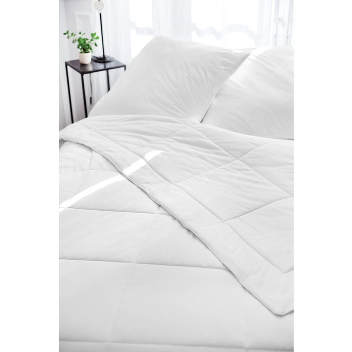 Ein ordentlich gemachtes Bett mit weißer Bettwäsche, Kissen und einer gesteppten Decke im hellen Schlafzimmer.