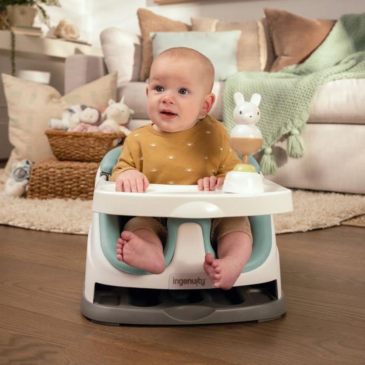 Ein Baby sitzt in einem Ingenuity-Babystuhl mit Tablett in einem hellen Wohnzimmer.