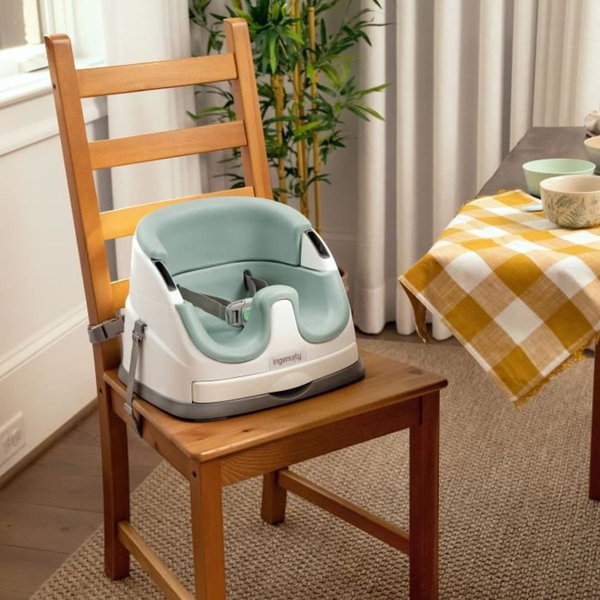 Ein mintgrüner und weißer Babysitz ist sicher auf einem Holzstuhl in einem hellen Esszimmer befestigt.