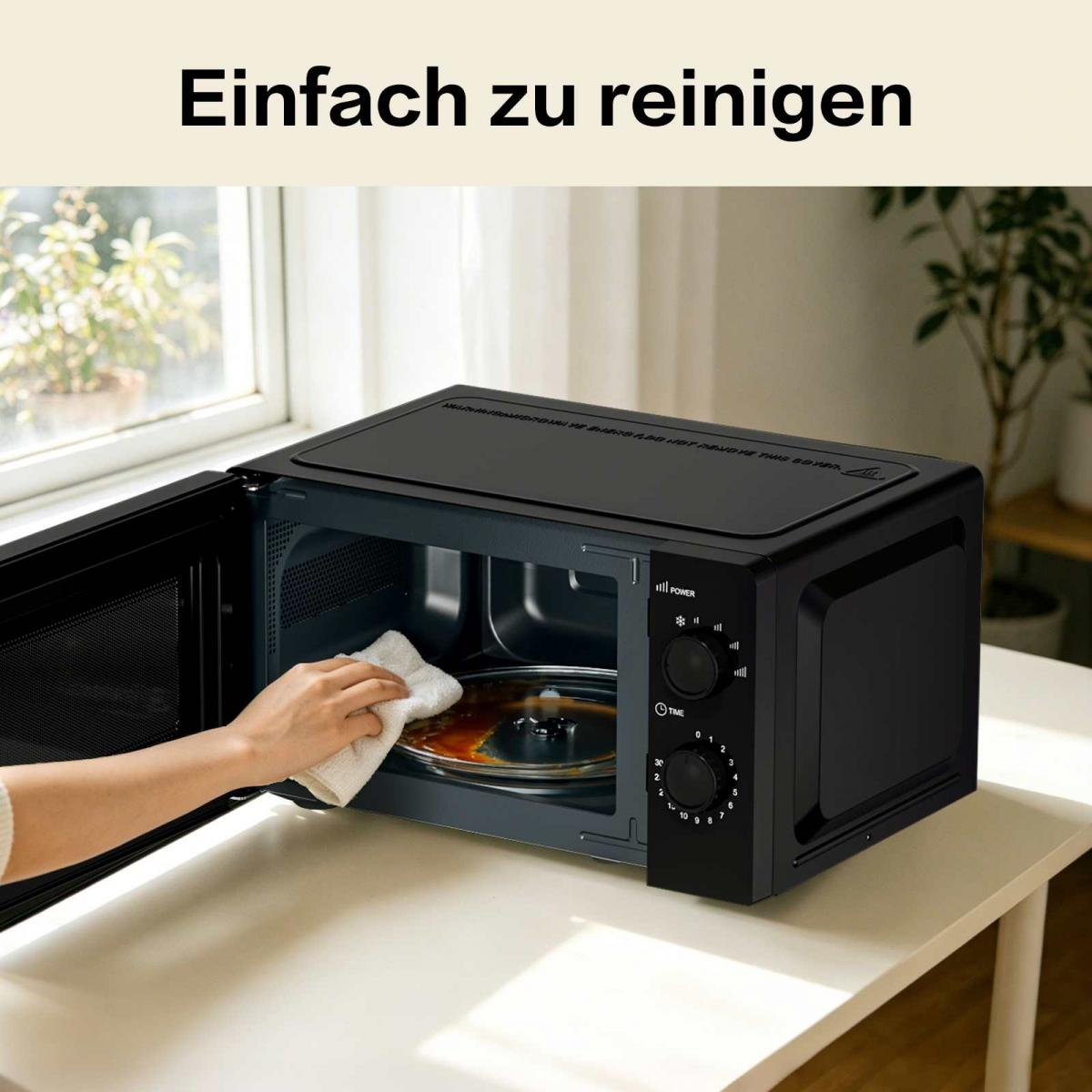 Eine Person wischt mit einem Tuch das Innere einer schwarzen Mikrowelle auf einem weißem Tisch.
