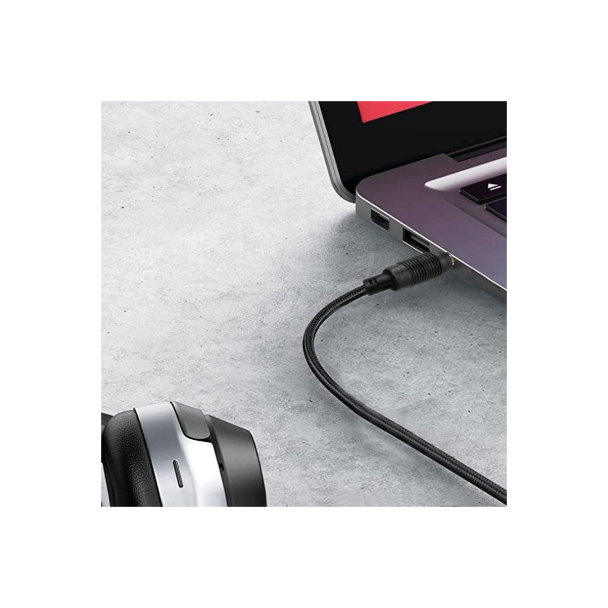 Un cable de audio está conectado a la toma de auriculares de un portátil apoyado en una superficie gris.