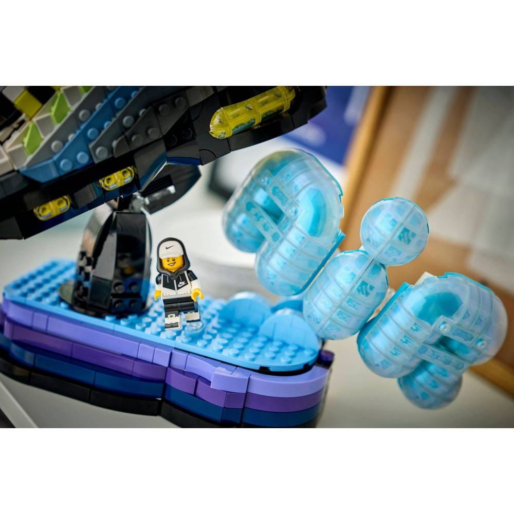 Minifigurka Lego stoi na niebieskiej podstawie obok półprzezroczystych niebieskich bąbelków i czarnego statku.