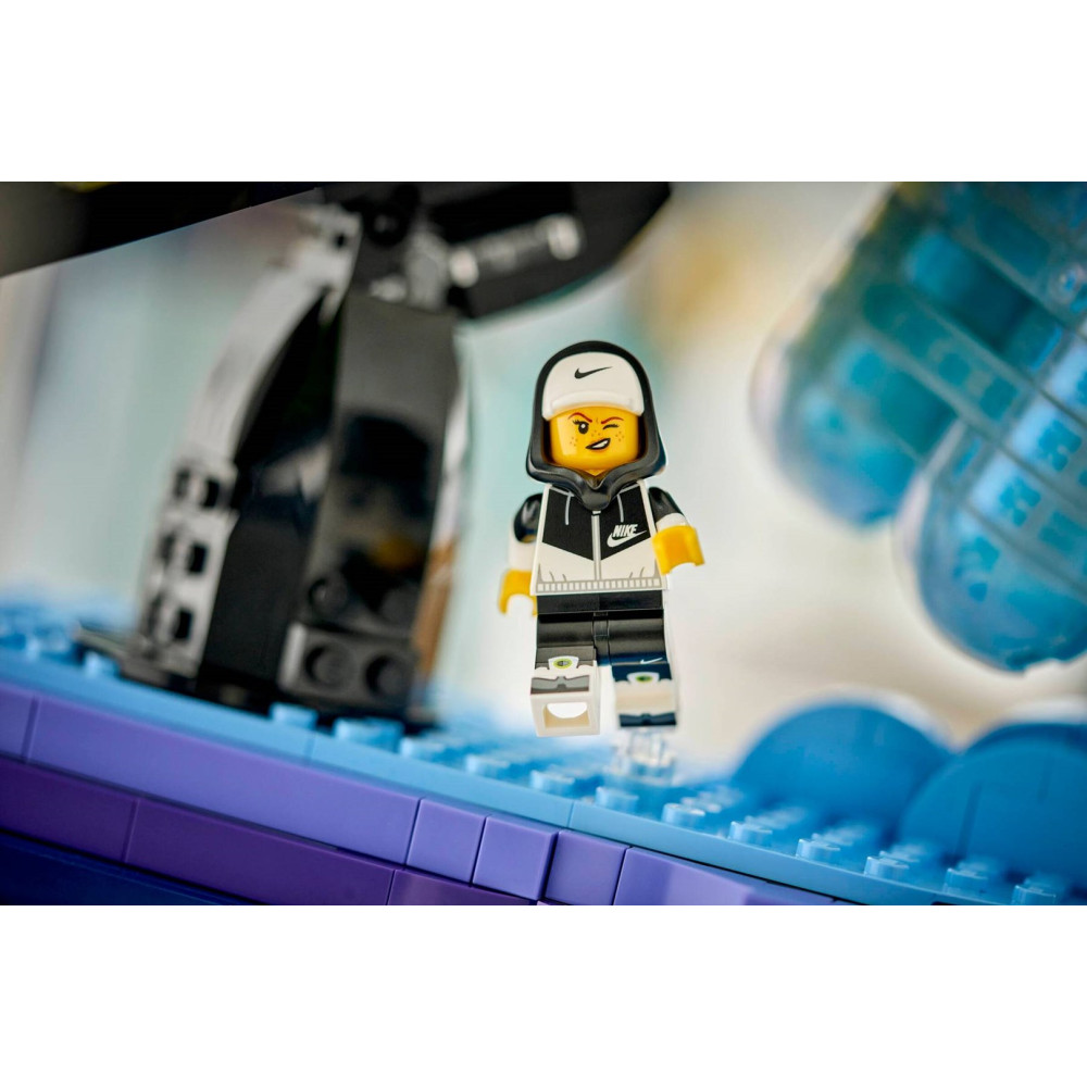 Minifigurka Lego w bluzie z kapturem i czapce stoi na niebieskich klockach.