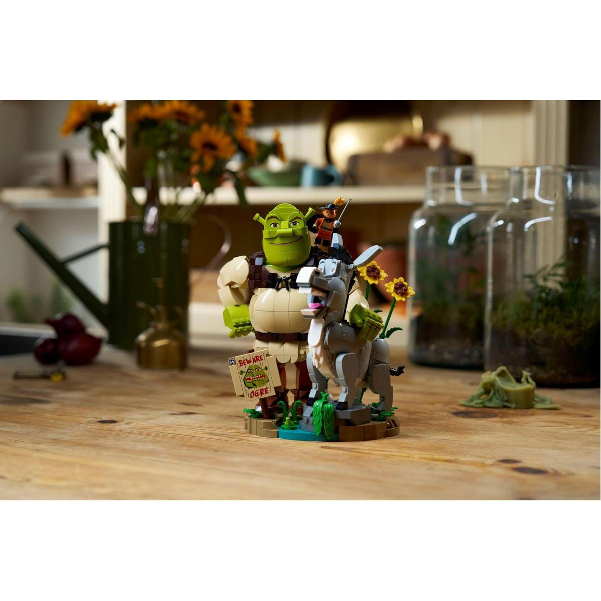 Figurki Lego przedstawiające Shreka, Osła i Kota w Butach stoją na drewnianym stole.
