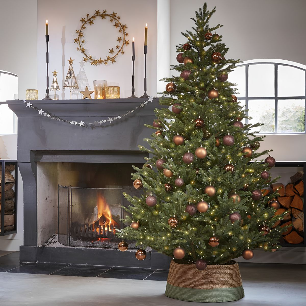 A decorated Christmas tree with bronze baubles in front of a fireplace.