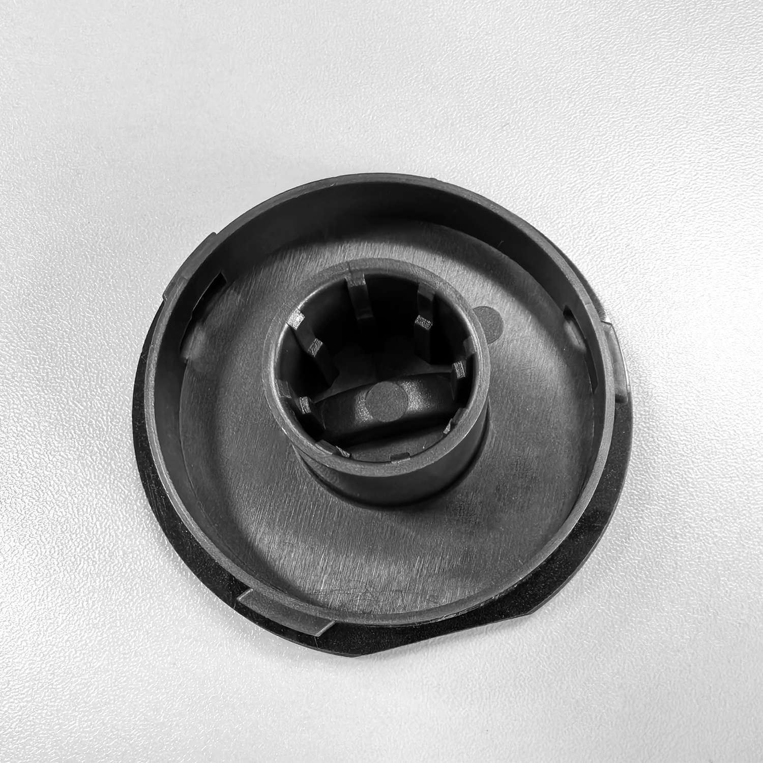 Un tappo di plastica nera con inserto cilindrico e alette interne, su superficie chiara.