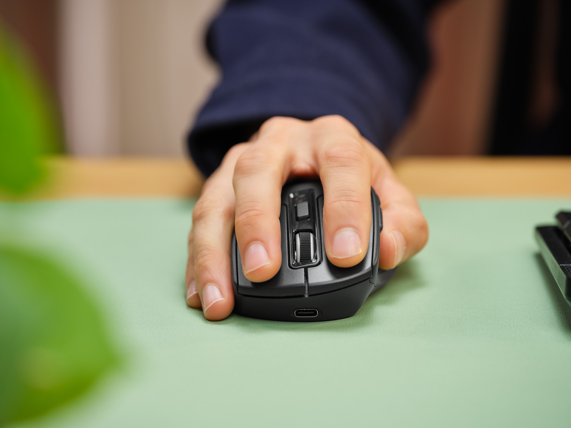 Eine Hand bedient eine schwarze Computermaus auf einer grünen Unterlage.