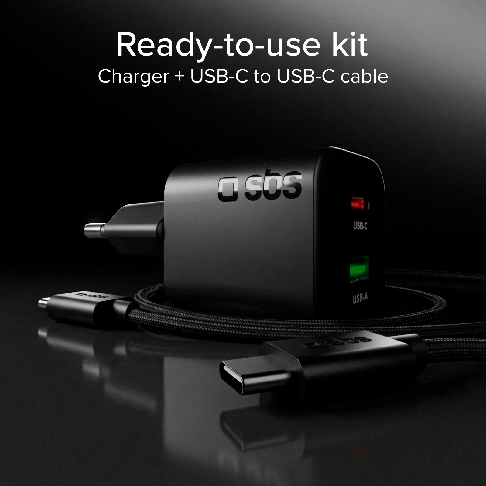 Un cargador negro SBS con puertos USB-C y USB-A, junto a un cable USB-C trenzado sobre fondo oscuro.