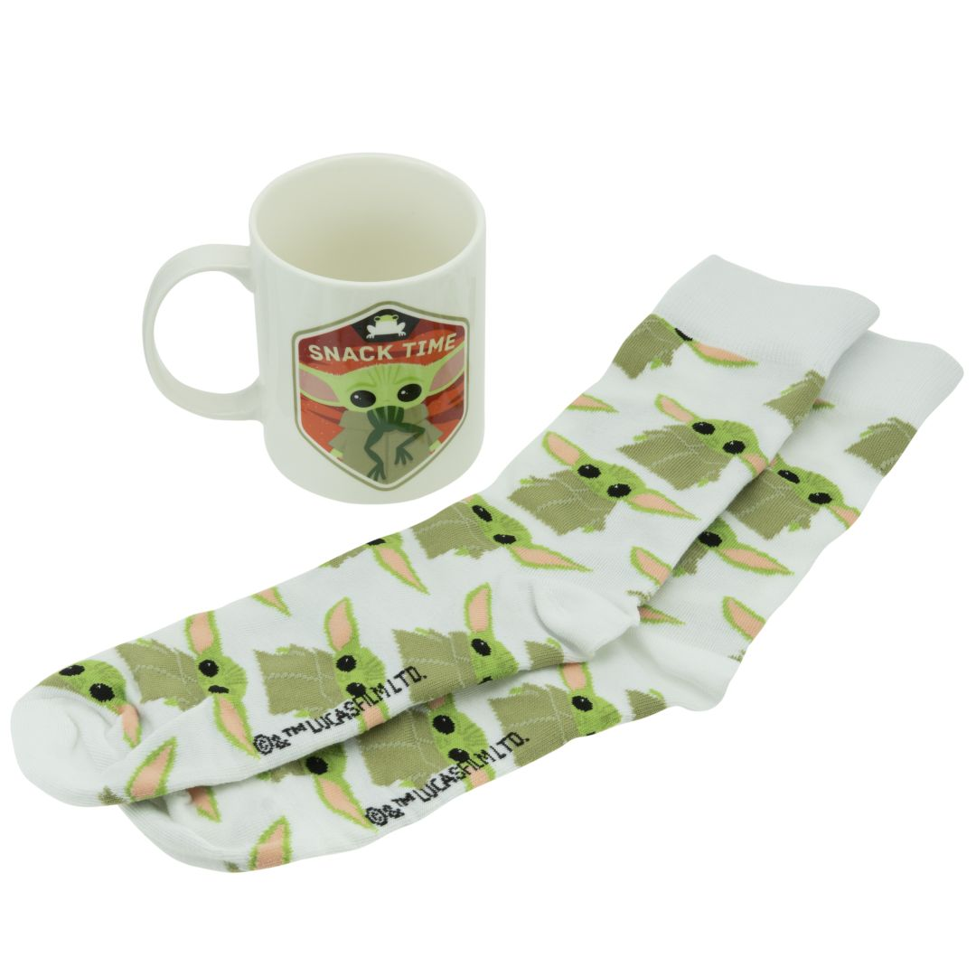 Ein weißer Becher mit Snack Time Grogu Motiv und ein Paar dazu passende weiße Socken mit Grogu Muster.