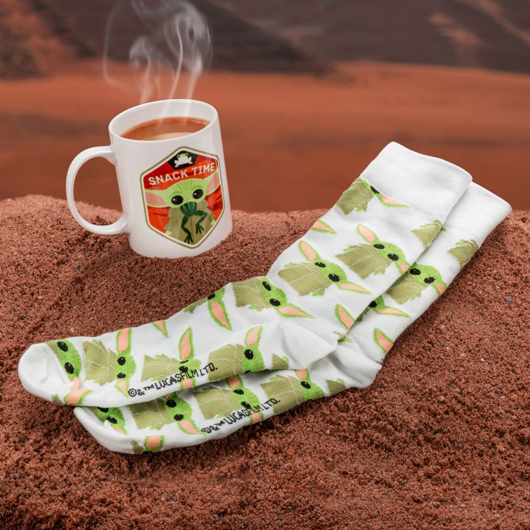 Eine weiße Tasse mit rauchendem Kaffee und Star Wars Socken liegen auf rotem Sand.