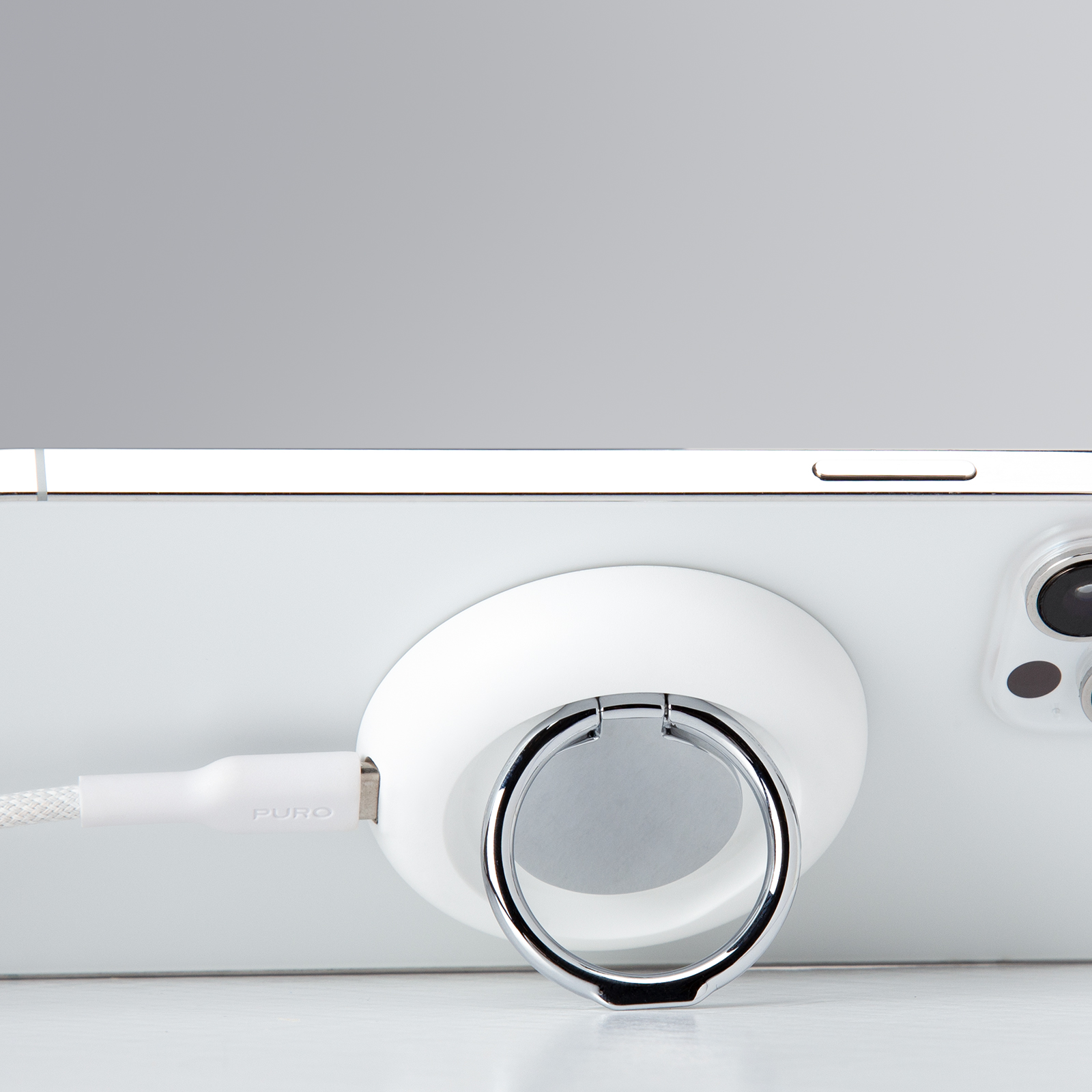 Un banco de energía blanco con un soporte de anillo está sujeto magnéticamente a la parte posterior de un teléfono inteligente blanco.