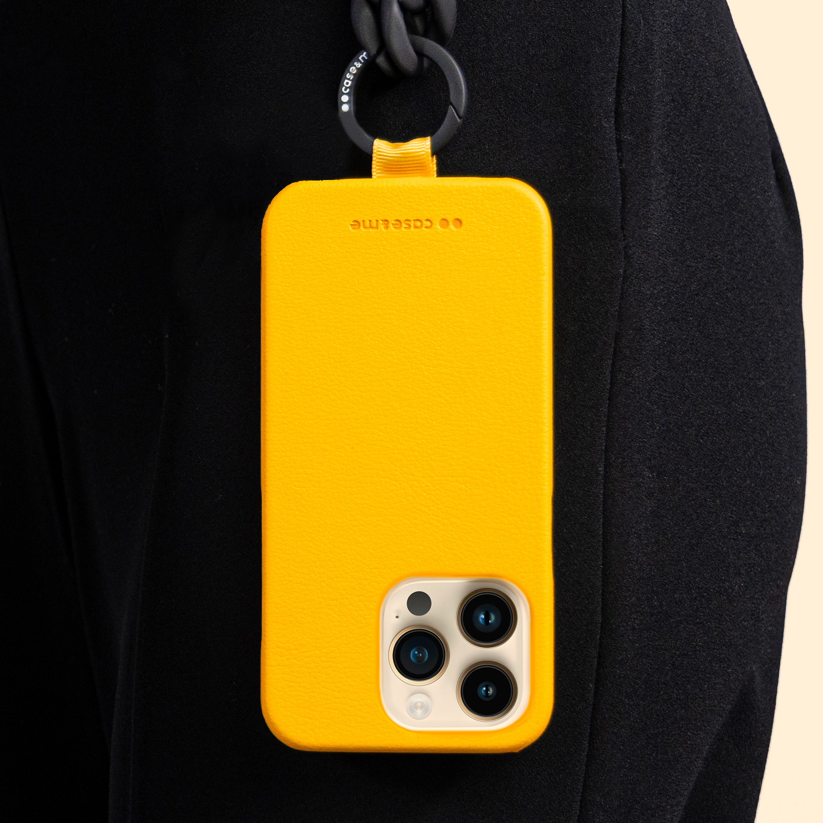 Una funda de teléfono amarilla brillante con tres lentes de cámara está sujeta a una correa negra.